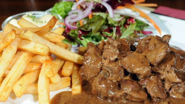 Een bord met stoofvlees, frietjes en een groentesalade
