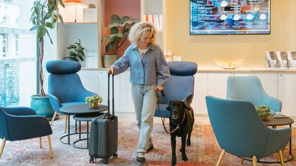 Lady with trolley and dog on leash walks towards room